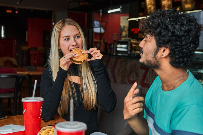 Two people in a restaurant, one eating a burger, representing common USA dining habits that confuse foreigners.