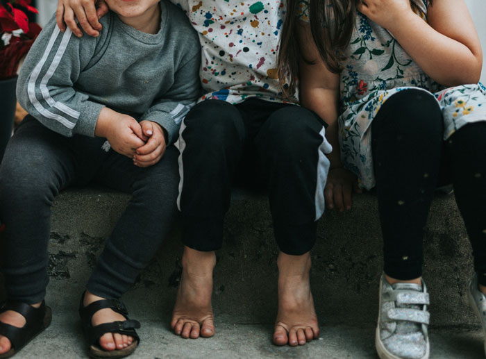 Three children sitting on a concrete step, wearing colorful and casual clothing, focusing on their shoes and pants.
