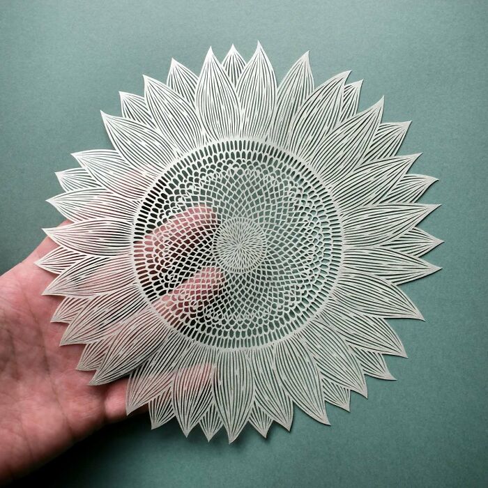 Intricate paper art design of a sunflower held against a green background, showcasing nature-inspired artistry.