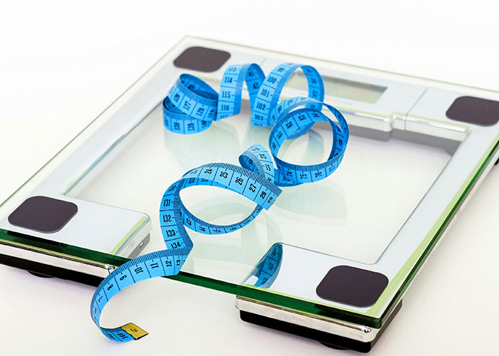 Digital scale with a blue tape measure, symbolizing challenges of being overweight.