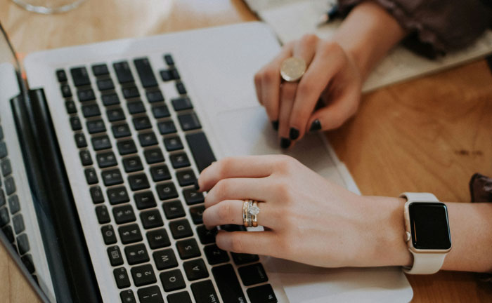 Person typing on a laptop, wearing a luxurious watch and ring, highlighting rich people's detachment from reality.