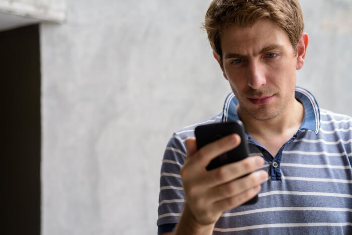 Man in striped shirt looking at his phone, appearing concerned or intrigued, related to worst first dates.