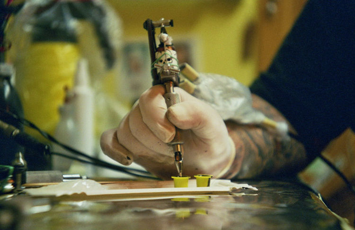 Tattoo artist's gloved hand holding a tattoo machine, preparing ink in a studio setting. Tattoo artist's gloved hand holding a tattoo machine, preparing ink in a studio setting.