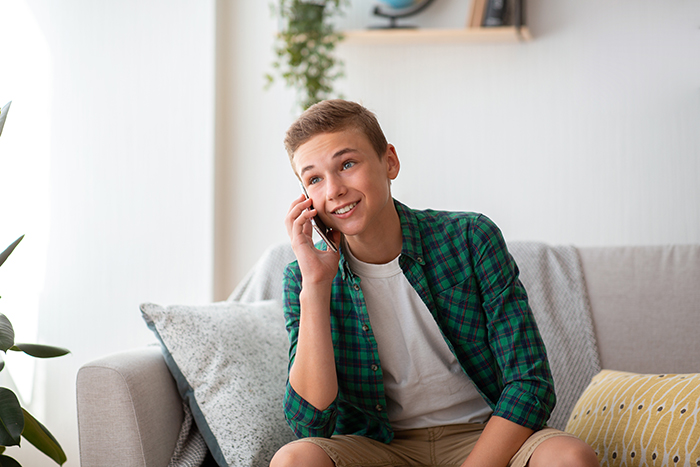 Teen sitting on a couch, talking on the phone, wearing a green plaid shirt, representing a story about proving someone isn't gay.