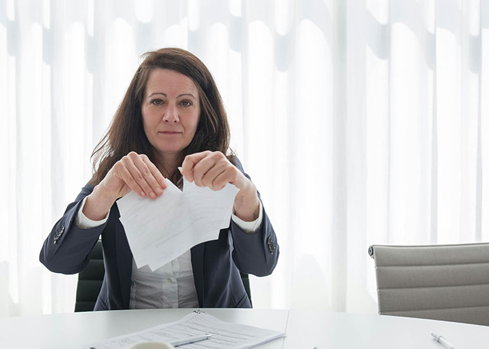 Woman tearing paper at a desk, symbolizing workplace revenge.