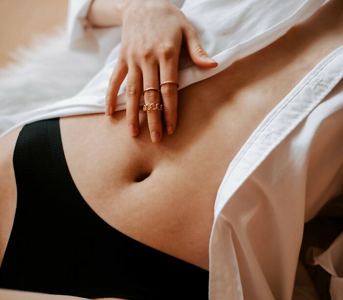 Close-up of a woman's abdomen, focusing on the female body, with a hand resting over a white shirt and black underwear.