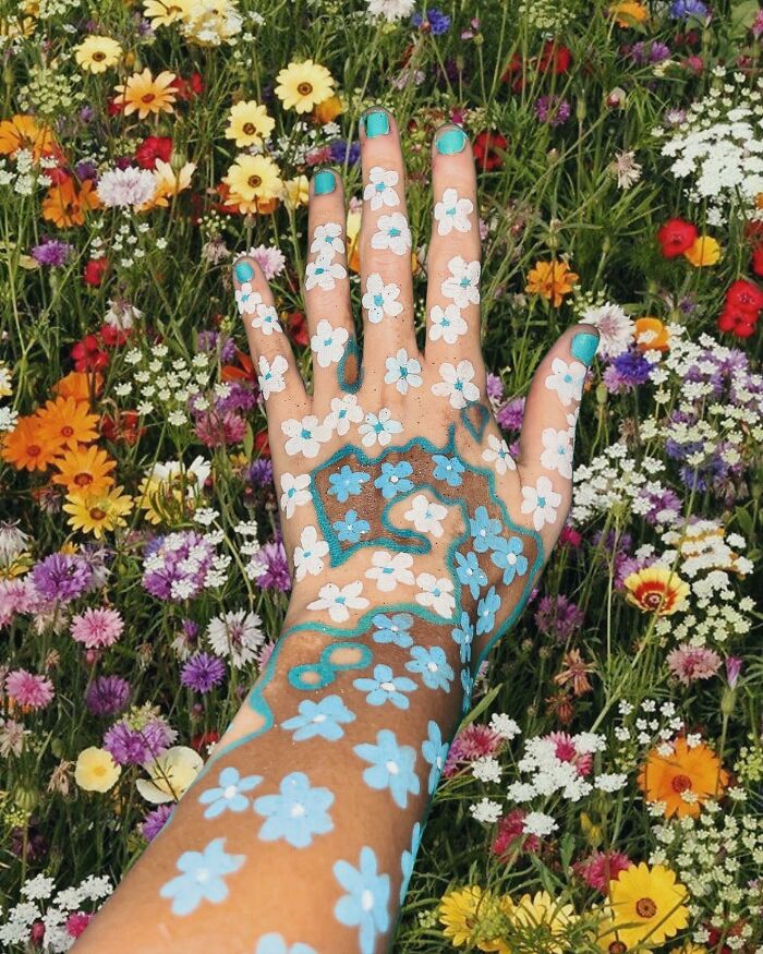 Hand with vitiligo transformed into art with blue and white flowers, set against a colorful field of wildflowers.