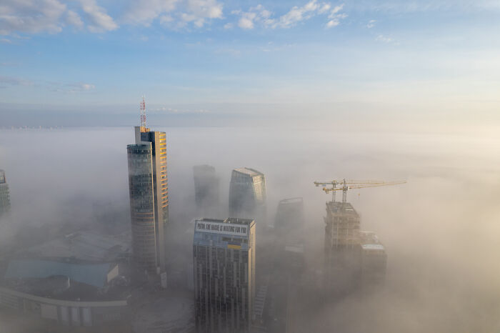 Bird's-eye view of Lithuania's cityscape with tall buildings emerging through the fog.