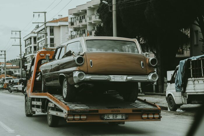 Tow truck carrying a classic car on a city street, highlighting professions that people dislike until they need help.