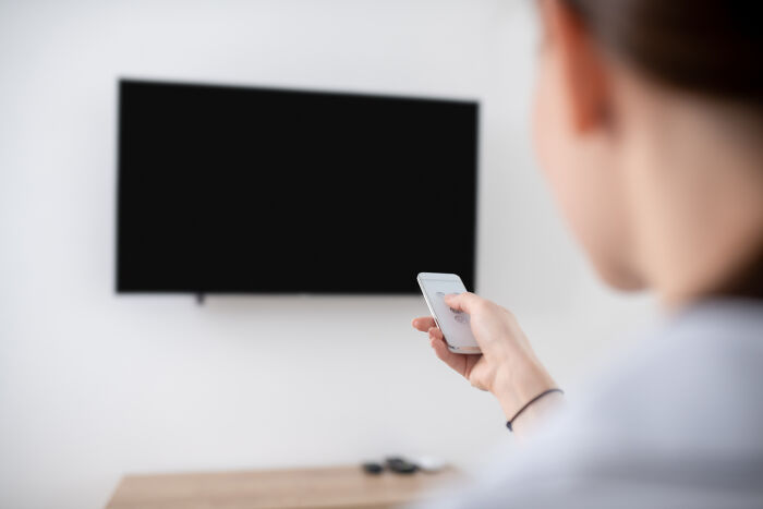 Person using remote control in front of a blank TV screen, indicating deep focus or unusual habits.