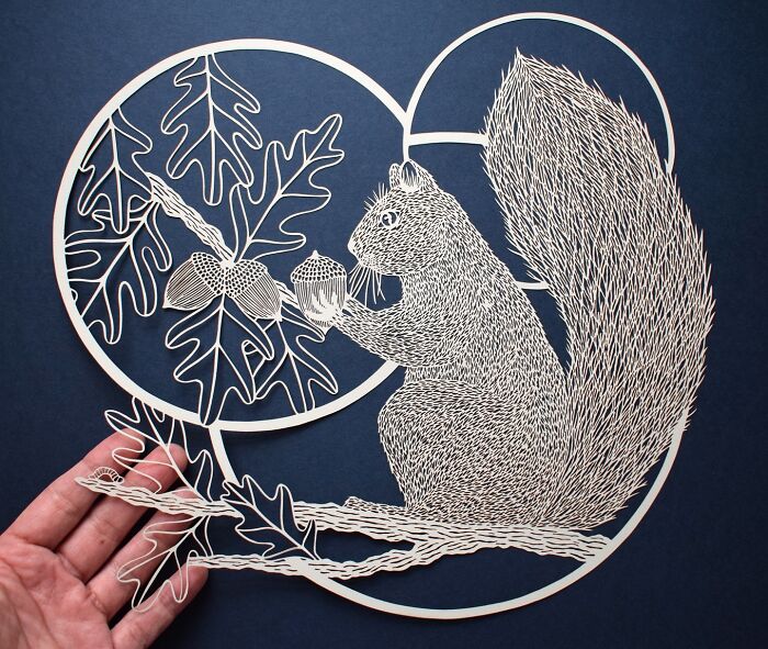Intricate paper art featuring a squirrel with acorns and leaves, showcasing nature-inspired design by Pippa Dyrlaga.