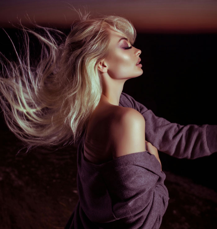 Blonde woman with wavy hair and closed eyes, symbolizing the prettiest girl theme, against a dark background.