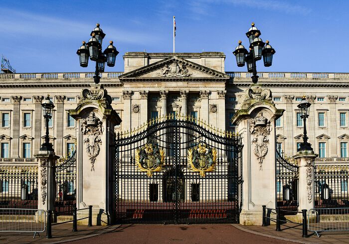 Buckingham Palace front view with ornate gates, pop culture landmark under blue sky.