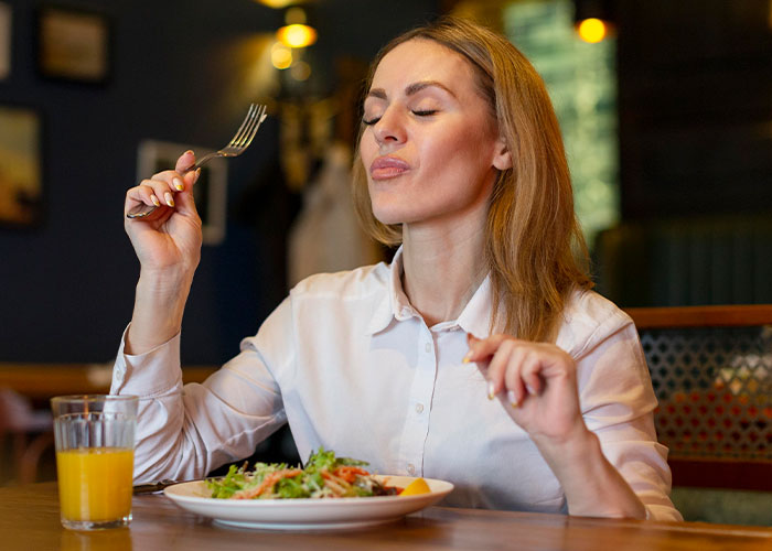 Woman dining at a restaurant table, enjoying her meal with a fork, a glass of orange juice beside her. Woman dining at a restaurant table, enjoying her meal with a fork, a glass of orange juice beside her.