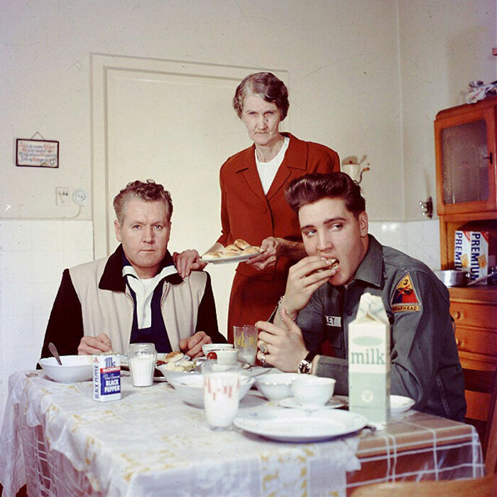 Three people in a vintage kitchen, enjoying a meal, with historical photo elements visible.