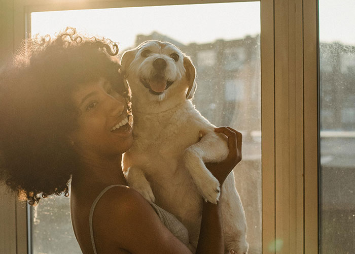 Woman joyfully holding a dog by a sunny window, reflecting wholesome happiness.
