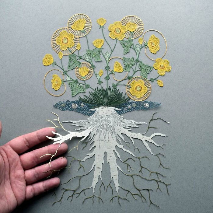 Intricate paper art design of flowers and roots with a hand for scale, inspired by nature.
