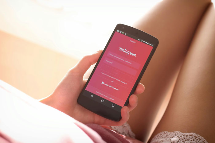 Person holding a smartphone displaying Instagram login screen, relevant to stories about the prettiest girl of high school.