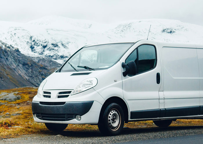 A white van parked on a mountain road with snow-covered peaks in the background, highlighting hilarious teacher stories.