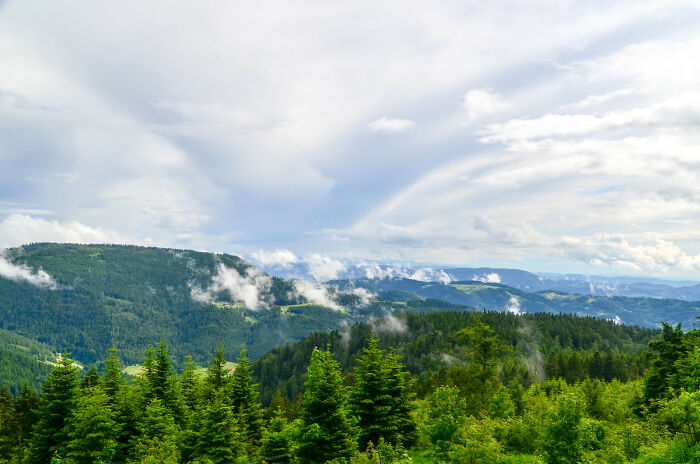 Lush green forested hills under a cloudy sky, showcasing natural wonders.