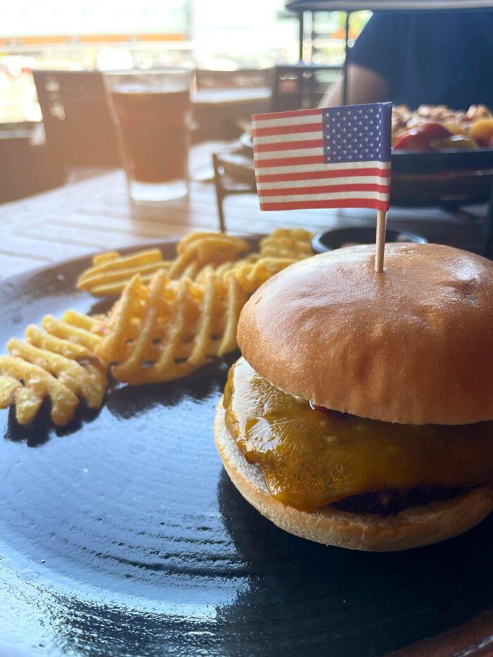 Burger with an American flag toothpick and waffle fries on a plate, highlighting a common USA thing.