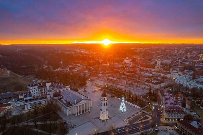 Aerial view of Lithuania's cityscape at sunset with vibrant sky and illuminated buildings.