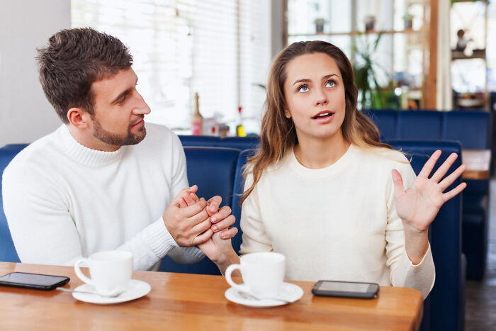 Man and woman in a cafe, discussing, both in white sweaters, two phones on the table, illustrating a humorous conversation.