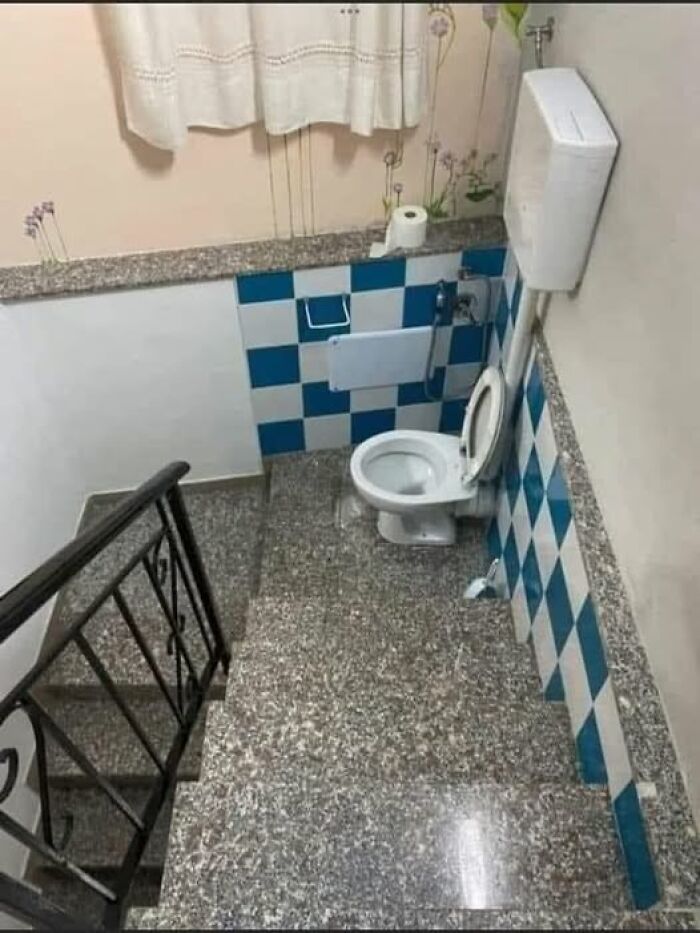 Weird image of a toilet at the bottom of a staircase, featuring blue and white checkered tiles.