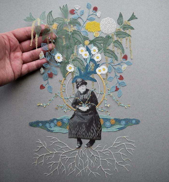 Hand showcasing nature-inspired intricate paper art with leaves and flowers above a vintage photo.