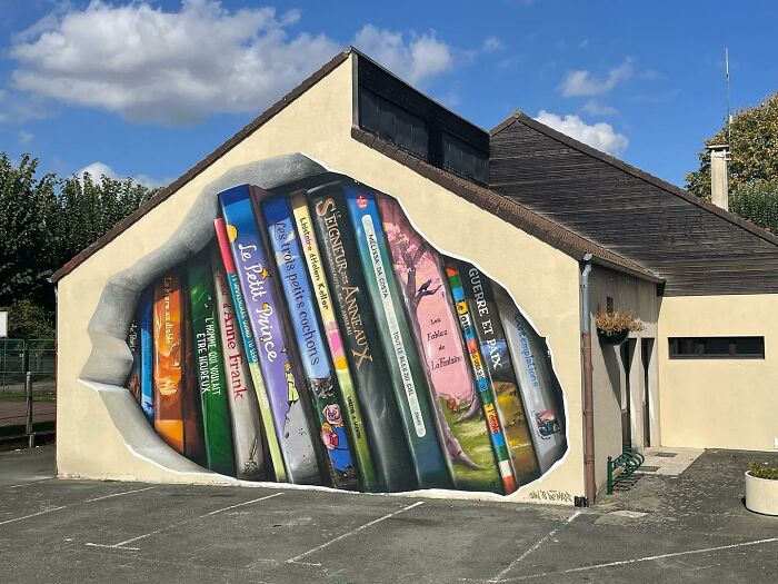 Mural of books on city wall by Jan Is De Man, showcasing stunning hyperrealistic illusions.