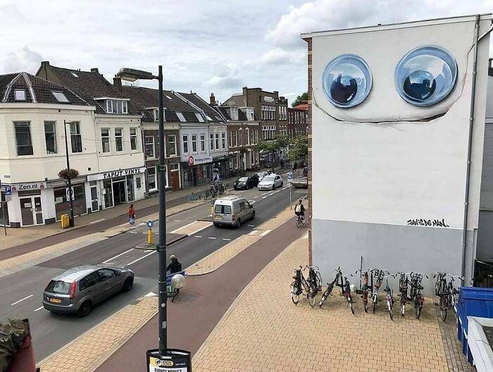 City wall mural by Jan Is De Man, featuring large, realistic eyes creating a hyperrealistic illusion on a street.