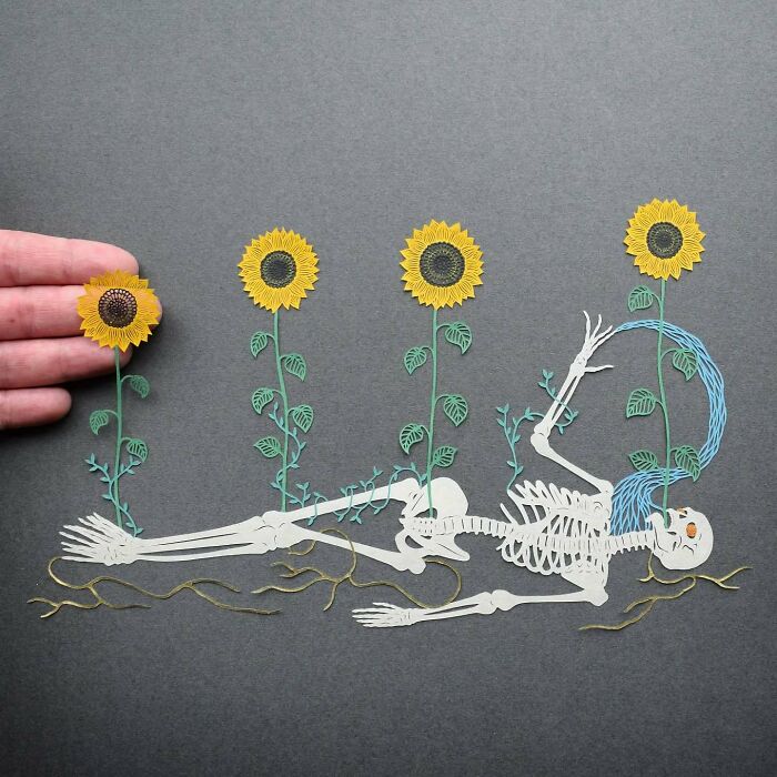 Intricate paper art design featuring a skeleton intertwined with sunflowers on a gray background.