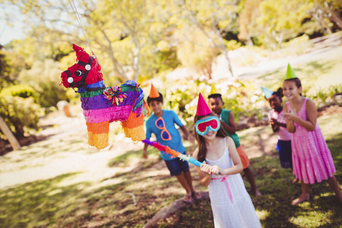 Children playing with a piñata, celebrating outdoors with party hats, featuring rules implemented for one individual.