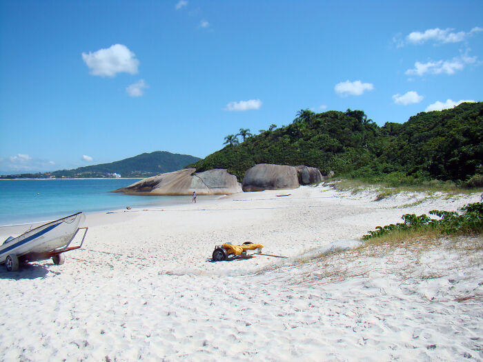 Retro Brazilian beach scene with white sand, a boat, and lush greenery under a clear blue sky.