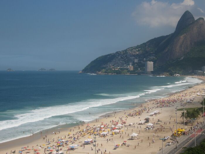 Retro Brazilian beach scene with people enjoying sun and sand, backed by lush mountains.
