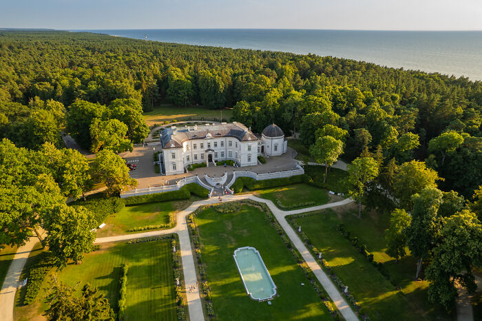 Lithuania bird’s-eye view of a grand estate surrounded by lush greenery and the distant sea.