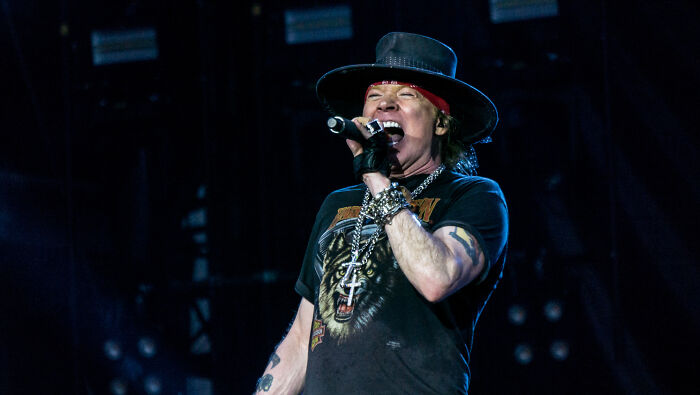 Musician performing on stage, wearing a hat and graphic t-shirt, symbolizing celebrity insights.