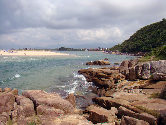 Retro Brazilian beach scene with rocky coastline, sandy beach, and overcast sky.