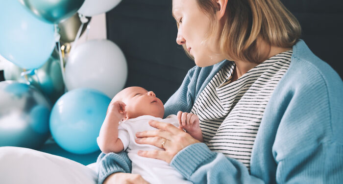 Woman cradling newborn, surrounded by balloons, showcasing American norms in parenting.