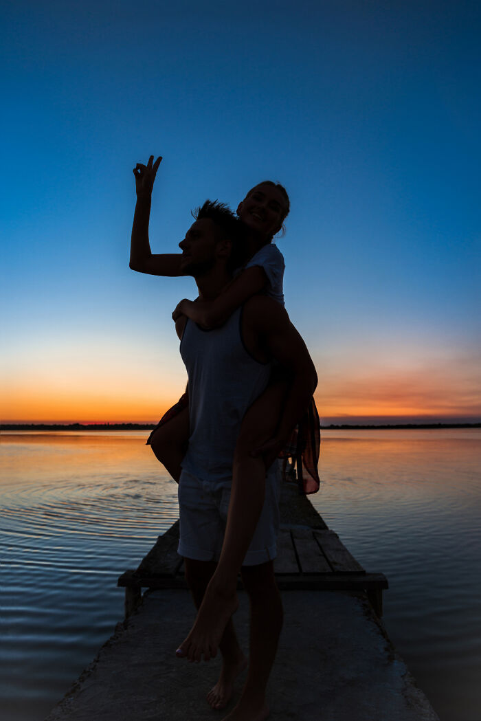 A couple enjoying a sunset on a pier, creating a silhouette against the vibrant evening sky.