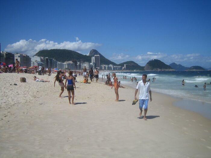 People enjoying a sunny day on a retro Brazilian beach with mountains and city skyline in the background.