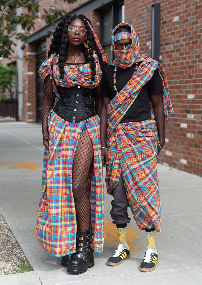 Two individuals showcasing bold fashion risks with colorful plaid outfits and unique accessories on a city street.