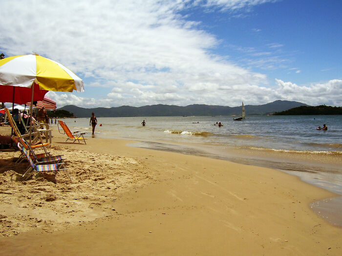 Retro Brazilian beach scene with chairs, umbrellas, and people enjoying the sun and ocean.