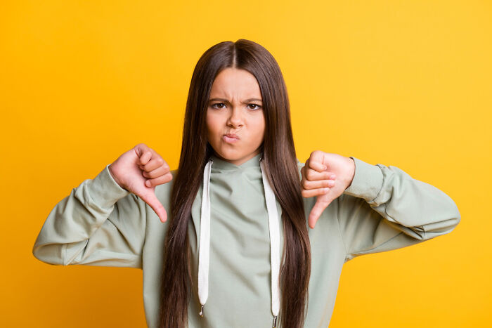 Person giving thumbs down gesture against a yellow background, expressing unattractive qualities non-physically.