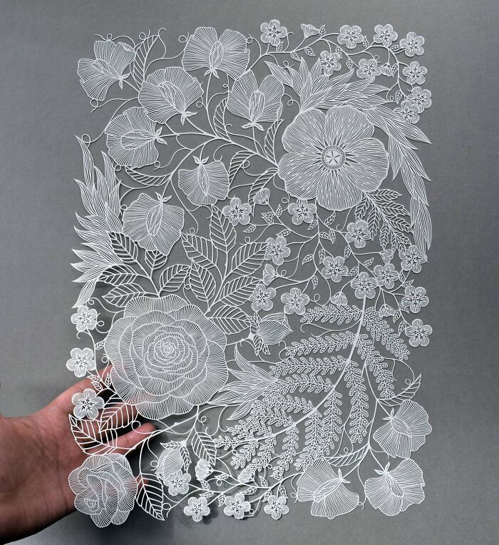 Intricate paper art design inspired by nature, featuring detailed flowers and leaves, held by a hand.