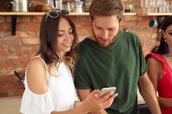 Couple on a date looking at a smartphone screen together in a cozy kitchen setting.