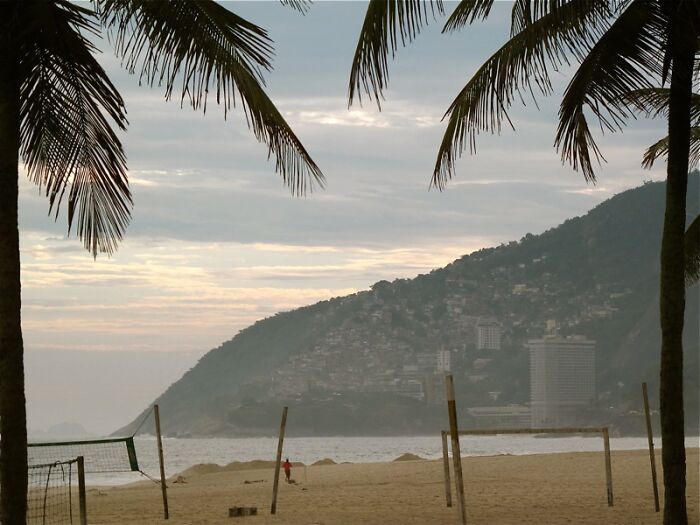 Retro Brazilian beach scene with palm trees, mountains, and a volleyball net, evoking sun and sand ambiance.