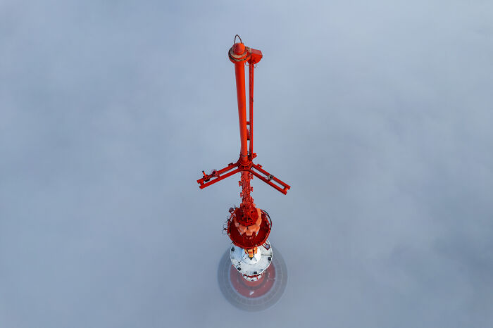Aerial view of a red and white tower in Lithuania emerging through the clouds.