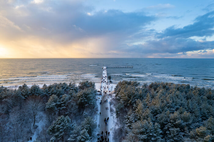 Aerial view of a snow-covered pier extending into the Baltic Sea, surrounded by forest in Lithuania.