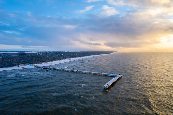 Aerial view of a pier extending into the sea, showcasing beautiful Lithuania landscapes under a cloudy sky.